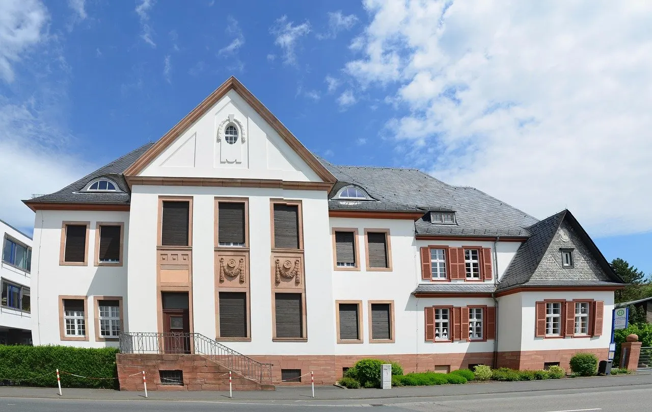Historisches Gebäude des Amtsgerichts Bad Camberg mit hellem Putz, Schieferdach und roten Fensterläden unter blauem Himmel