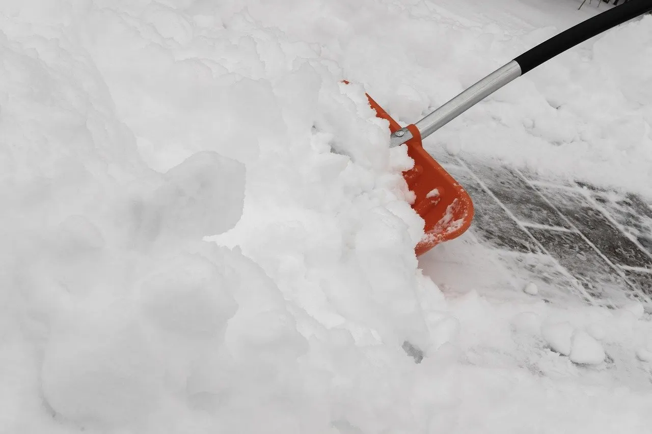 Orange Schneeschaufel schiebt eine dicke Schneeschicht von einer gepflasterten Fläche, dahinter ist der Belag schon teils frei