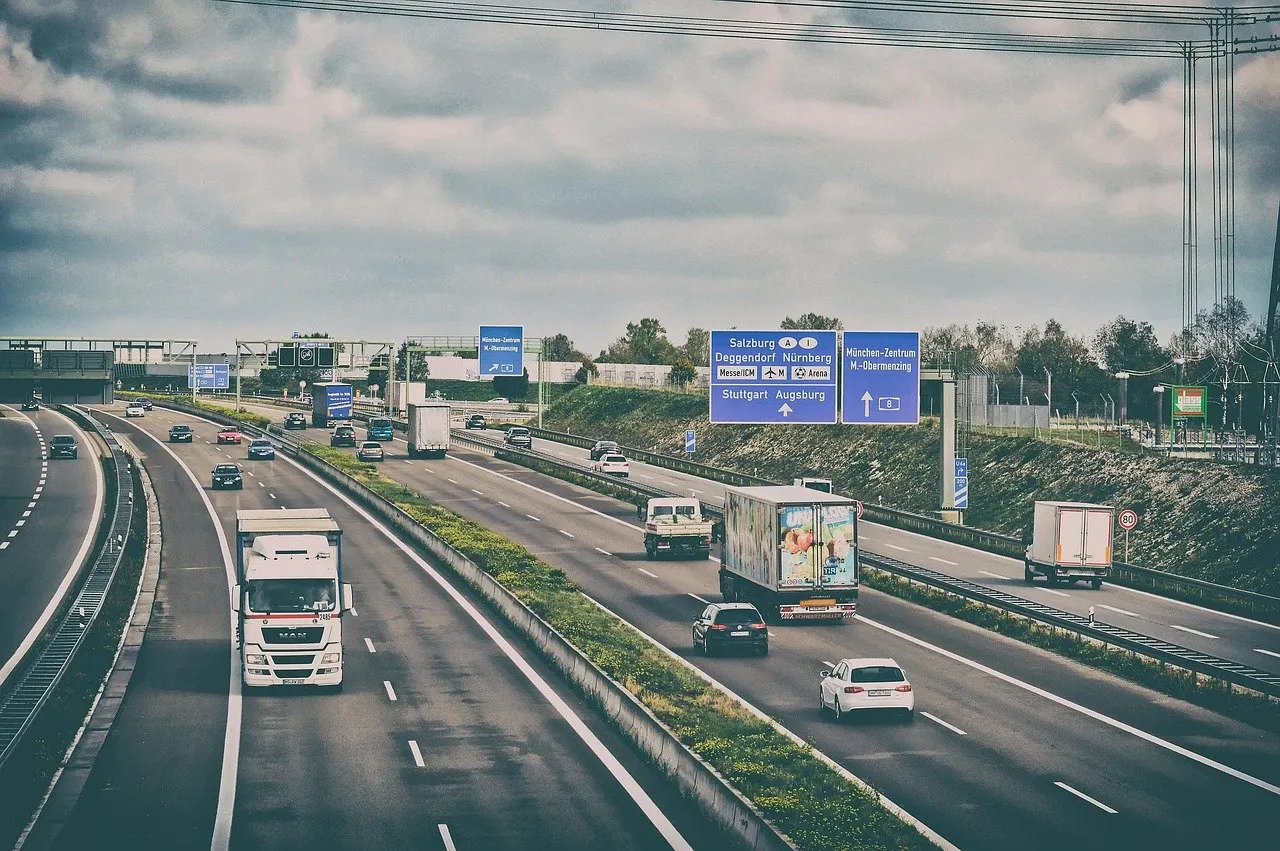 Mehrspurige Autobahn bei München mit Lkw, Transportern und Pkw, darüber blaue Wegweiser Richtung Salzburg, Nürnberg und Stuttgart
