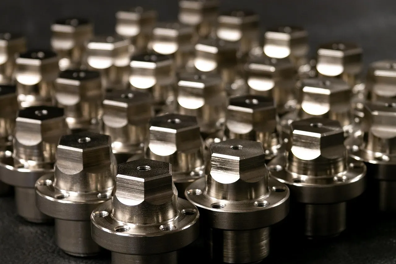 Reihen gleicher CNC-Drehfrästeile aus blankem Metall mit Sechskantkopf und gebohrtem Flansch auf dunkler Unterlage